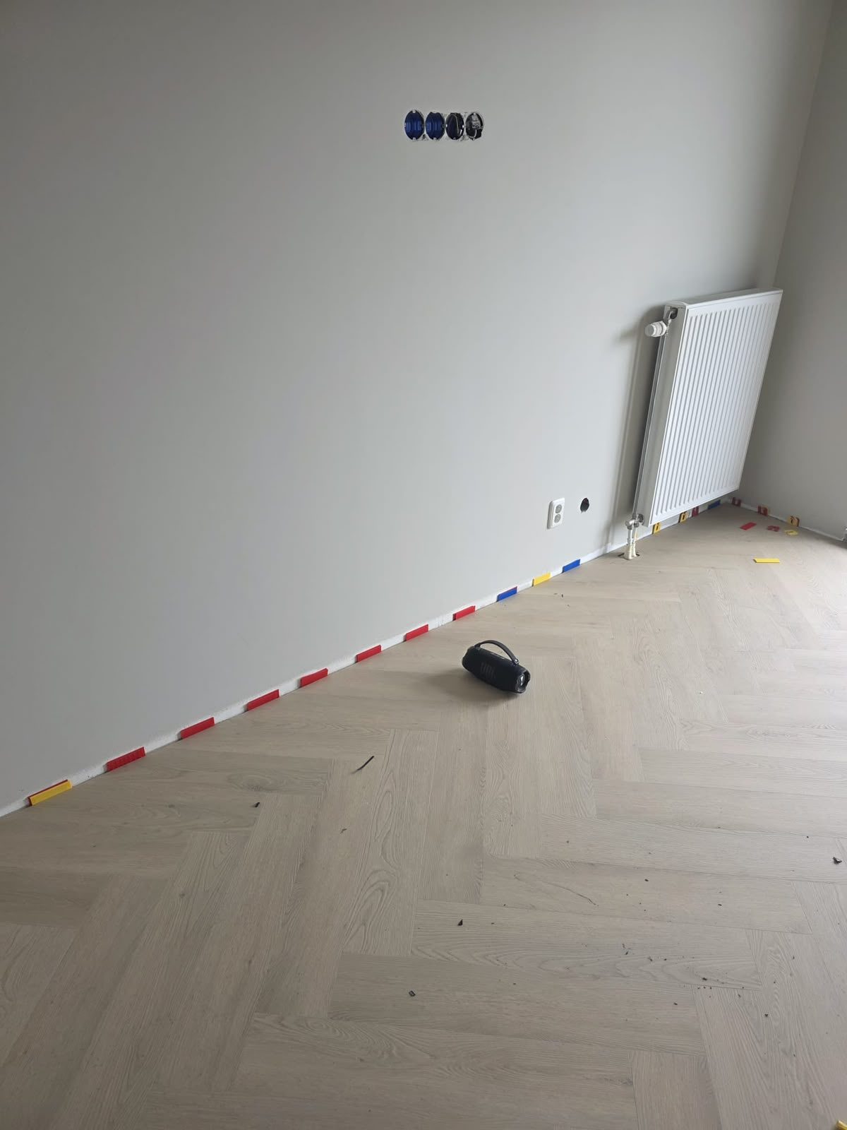 Licht eiken PVC visgraatvloer in een lege nieuwbouwkamer, met uitzetruimte langs de muur